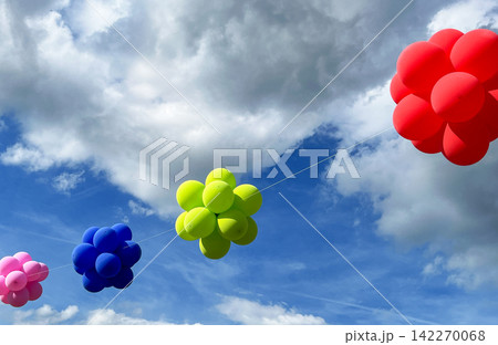 Colorful balloon clusters against a cloudy blue sky 142270068