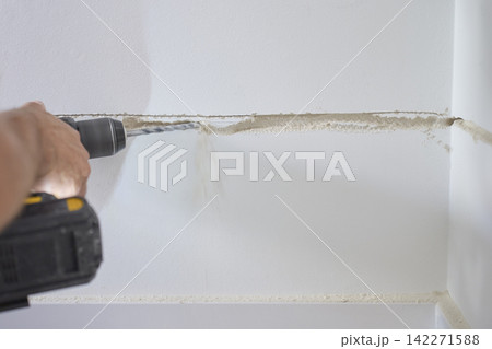 Person drills along channel in interior wall while dust falls from surface Person drills along channel in interior wall while dust falls from surface 142271588