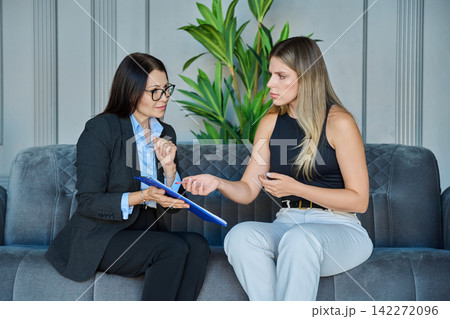 Female psychologist holding clipboard and looking at emotional patient during therapy session 142272096