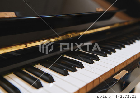Close-up photograph of an upright piano showing black and white keys, glossy finish and warm lighting - evokes music practice, teaching and classical atmosphere. Close-up photograph of an upright piano showing black and white keys, glossy finish and warm lighting - evokes music practice, teaching and classical atmosphere. 142272323