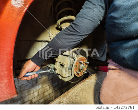 Mechanic working on a vehicle's suspension and brake system, using a ratchet wrench to maintain the brake calliper and rotor, performing routine car service in a garage 142272761