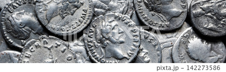 Panoramic view of ancient Roman silver coins in a pile. Macro photography of antique metallic currency with embossed emperor profiles. History, money and archaeology concept Panoramic view of ancient Roman silver coins in a pile. Macro photography of antique metallic currency with embossed emperor profiles. History, money and archaeology concept 142273586