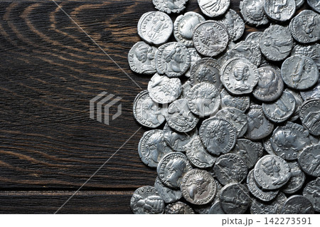 Pile of ancient Roman silver coins on a old wooden table. Historical currency and vintage money flat lay. Top view of antique money, background. 142273591