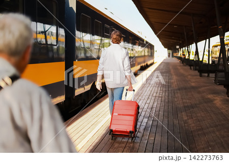 passenger with luggage is walking on the train station platform for departure. The man pulls a red suitcase to start his travel journey. passenger with luggage is walking on the train station platform for departure. The man pulls a red suitcase to start his travel journey. 142273763