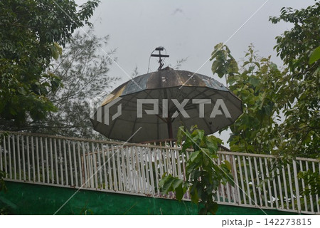 Large grey umbrella structure installed above white fence and trees Large grey umbrella structure installed above white fence and trees 142273815