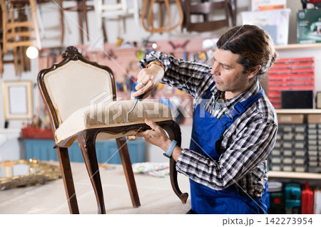 Portrait of middle-aged skillful repairman carpenter renovating chair furniture using tools in woodwork studio Portrait of middle-aged skillful repairman carpenter renovating chair furniture using tools in woodwork studio 142273954