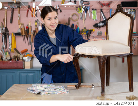 Young female carpenter working on making vintage chair in workshop 142274071