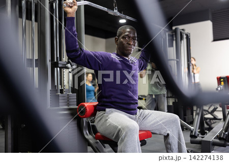 African man doing exercises on lat pull down machine in gym African man doing exercises on lat pull down machine in gym 142274138
