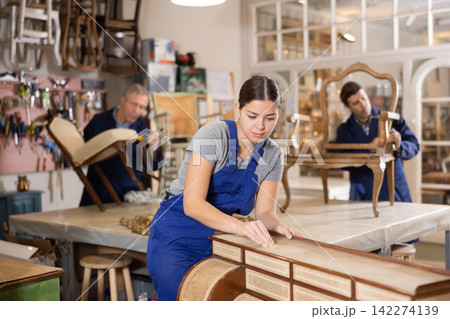 Experienced woman restorer restores the cover of vintage chest of drawers Experienced woman restorer restores the cover of vintage chest of drawers 142274139