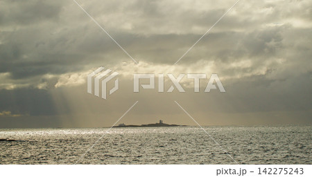 Lighthouse on island with sunbeams breaking through clouds 142275243