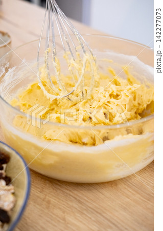 Dough preparation. Home cuisine. Kitchen metal whisk mixing thick yellow butter pastry recipe mass in glass bowl on culinary countertop. Dough preparation. Home cuisine. Kitchen metal whisk mixing thick yellow butter pastry recipe mass in glass bowl on culinary countertop. 142277073