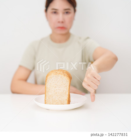 Unhappy woman showing thumbs down gesture and refusing to eat bread. concept of gluten intolerance, gluten sensitivity, carb loading concerns, or a disliking for unhealthy dietary habits Unhappy woman showing thumbs down gesture and refusing to eat bread. concept of gluten intolerance, gluten sensitivity, carb loading concerns, or a disliking for unhealthy dietary habits 142277831