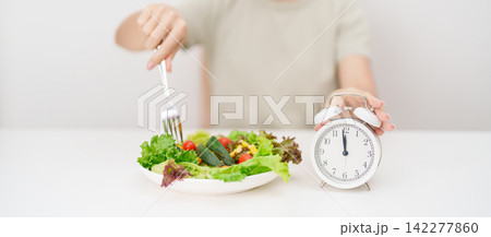 happy smiling woman with fresh organic vegetables plate and alarm clock. intermittent fasting, IF, meal time, nutrition, weight loss, clean eating, Healthy food eating, Wellness, dieting and lifestyle happy smiling woman with fresh organic vegetables plate and alarm clock. intermittent fasting, IF, meal time, nutrition, weight loss, clean eating, Healthy food eating, Wellness, dieting and lifestyle 142277860