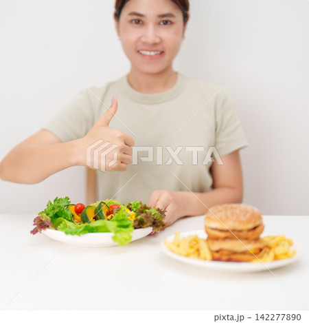 happy woman choose vegetables Salad and thumbs up gesture. Healthy and Unhealthy Food Choice, Calories and Nutrition of vegetables and Hamburger. dieting, weight loss control, junk food and lifestyle 142277890