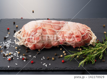 スレートプレートに置かれたネット入り生豚肉ブロック ローズマリーとスパイス添え 黒背景 142278929