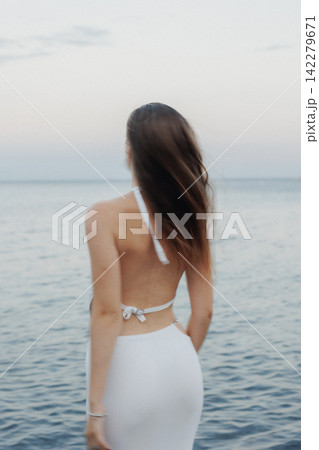 Woman stands by calm sea at dusk Woman stands by calm sea at dusk 142279671
