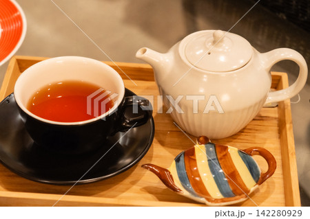 木製トレーに並ぶ黒いカップの紅茶と白いティーポット 木製トレーに並ぶ黒いカップの紅茶と白いティーポット 142280929
