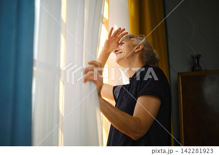 Person looking out window while holding curtains in bright indoor space during daylight hours Person looking out window while holding curtains in bright indoor space during daylight hours 142281923