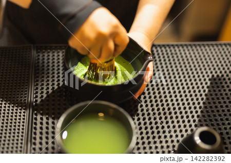 Barista whisking matcha green tea using a traditional bamboo whisk in ceramic bowl. Barista whisking matcha green tea using a traditional bamboo whisk in ceramic bowl. 142282392