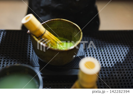 Matcha green tea with traditional bamboo whisk resting inside a ceramic bowl. Matcha green tea with traditional bamboo whisk resting inside a ceramic bowl. 142282394