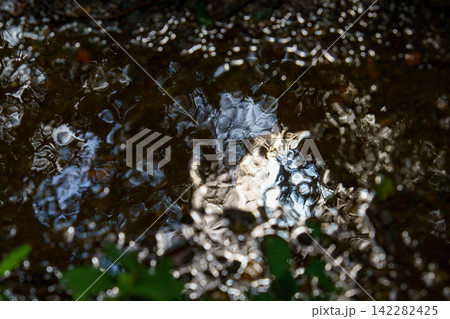 雨あがりの流れる水溜りに反射する光 142282425