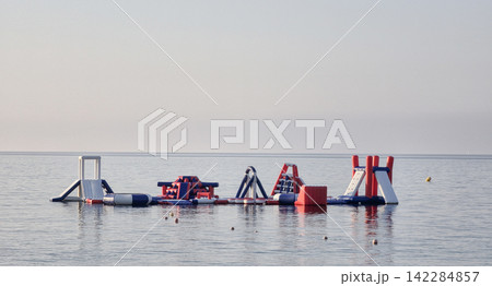 Inflatable water park obstacle course floating on the calm sea surface at sunset. 142284857
