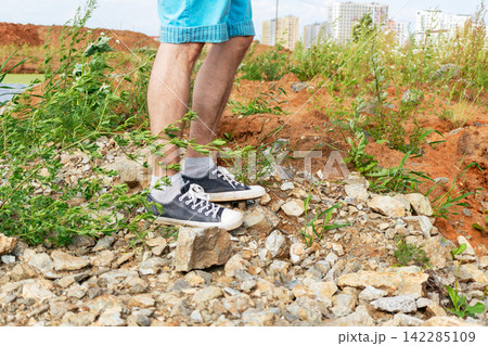 Man walking across a rocky urban construction site with weeds and exposed soil. Outdoor exploration, land development and environmental change concept. 142285109
