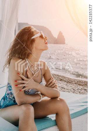 Woman beach vacation sitting on a sunbed by the sea at sunset enjoying a relaxing summer holiday at a resort 142285377