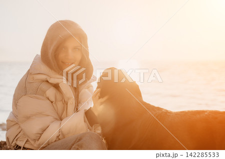 Dog woman companionship smiling woman petting a black dog on a sunny beach shore at golden hour. Dog woman companionship smiling woman petting a black dog on a sunny beach shore at golden hour. 142285533