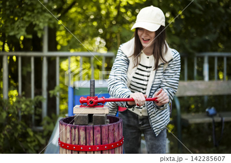 Smiling woman operating a manual grape press, illustrating a workshop moment and sustainable practices in the wine industry. 142285607