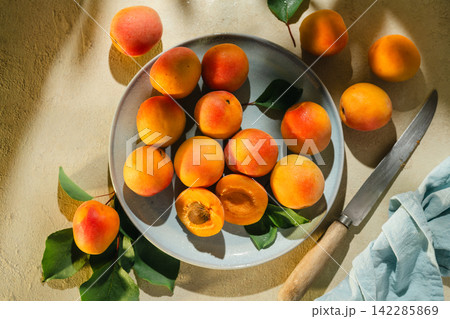 Fresh ripe apricots on ceramic plate with leaves, knife and halved fruit in sunlight Fresh ripe apricots on ceramic plate with leaves, knife and halved fruit in sunlight 142285869