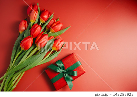 Celebration background. Mothers' day. Red tulips with a gift box. Red background, copy space. 142285925