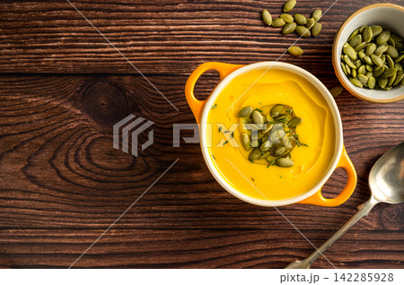 Pumpkin soup in orange ceramic bowl, wooden background. Autumn food Pumpkin soup in orange ceramic bowl, wooden background. Autumn food 142285928