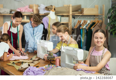 Sewing lesson - a group of teenage children learn to sew on sewing machine and cut fabric Sewing lesson - a group of teenage children learn to sew on sewing machine and cut fabric 142288087