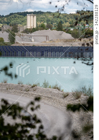 Vertical floating solar panels on the Gilching quarry lake in Bavaria, Germany, beside a gravel and crushing plant, renewable energy infrastructure, industrial landscape and innovative clean Vertical floating solar panels on the Gilching quarry lake in Bavaria, Germany, beside a gravel and crushing plant, renewable energy infrastructure, industrial landscape and innovative clean 142288129