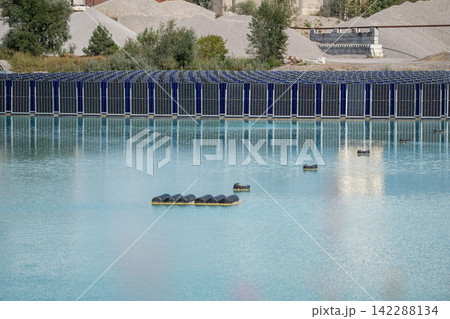 Vertical floating solar panels on the Gilching quarry lake in Bavaria, Germany, beside a gravel and crushing plant, renewable energy infrastructure, industrial landscape and innovative clean Vertical floating solar panels on the Gilching quarry lake in Bavaria, Germany, beside a gravel and crushing plant, renewable energy infrastructure, industrial landscape and innovative clean 142288134