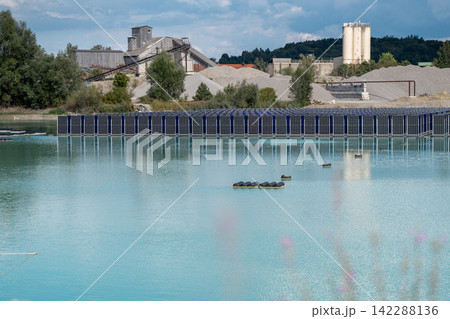 Vertical floating solar panels on the Gilching quarry lake in Bavaria, Germany, beside a gravel and crushing plant, renewable energy infrastructure, industrial landscape and innovative clean Vertical floating solar panels on the Gilching quarry lake in Bavaria, Germany, beside a gravel and crushing plant, renewable energy infrastructure, industrial landscape and innovative clean 142288136