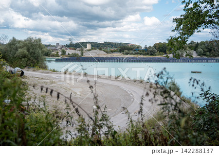 Vertical floating solar panels on the Gilching quarry lake in Bavaria, Germany, beside a gravel and crushing plant, renewable energy infrastructure, industrial landscape and innovative clean Vertical floating solar panels on the Gilching quarry lake in Bavaria, Germany, beside a gravel and crushing plant, renewable energy infrastructure, industrial landscape and innovative clean 142288137