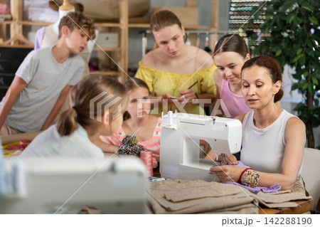 Woman teacher sews product surrounded by students Woman teacher sews product surrounded by students 142288190