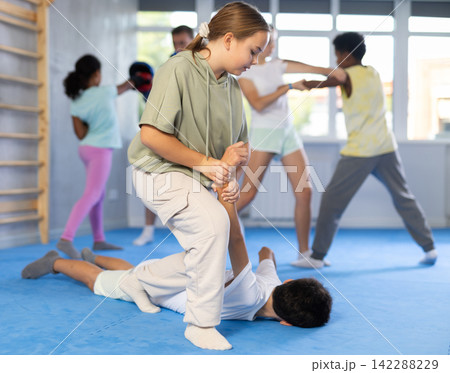 Tween girl applying armlock to face-down boy in mock fight at self-defense classes 142288229