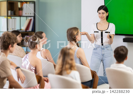 Female teacher holding a remote control and speaking to student audience Female teacher holding a remote control and speaking to student audience 142288230