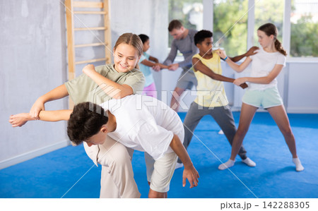 Preteen girl performing elbow and knee strikes while blocking arm of boy in mock fight Preteen girl performing elbow and knee strikes while blocking arm of boy in mock fight 142288305