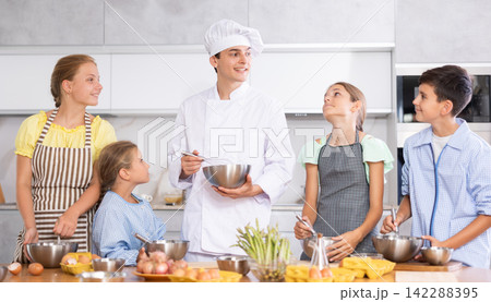Friendly young chef running culinary courses for group of children Friendly young chef running culinary courses for group of children 142288395