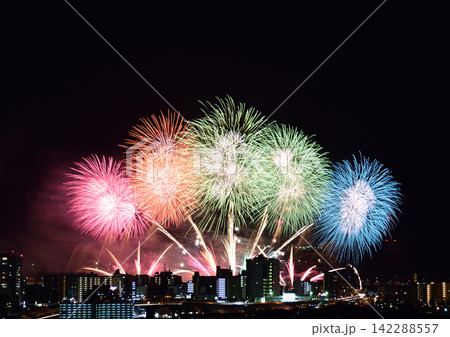 夏の夜空に輝くカラフルな連発花火と街並みのシルエット 142288557