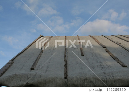 Rustic wooden rooftop of old village house under blue cloudy sky 142289520