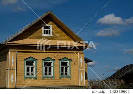 Traditional yellow wooden village house under beautiful blue cloudy sky Traditional yellow wooden village house under beautiful blue cloudy sky 142289602