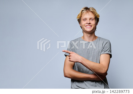 Portrait of smiling teenage boy pointing thumb at copy space Portrait of smiling teenage boy pointing thumb at copy space 142289773