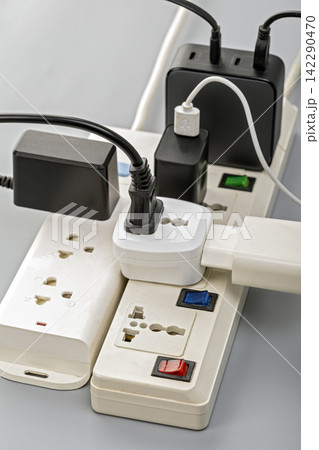 Close-up of overloaded electrical power strips with multiple plugs, adapters, and USB chargers connected in a risky daisy chain arrangement, illustrating electrical hazard concept Close-up of overloaded electrical power strips with multiple plugs, adapters, and USB chargers connected in a risky daisy chain arrangement, illustrating electrical hazard concept 142290470