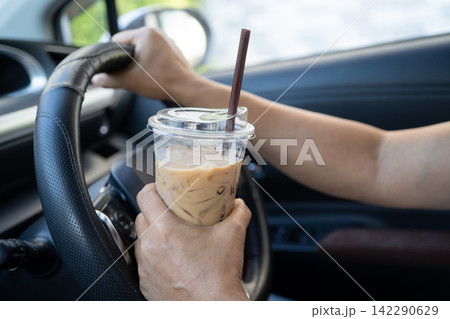 Asian lady holding ice coffee to eat in car, dangerous and risk an accident. Asian lady holding ice coffee to eat in car, dangerous and risk an accident. 142290629