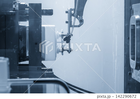 Automatic material handling of plastic parts from injection machine using robotic arm in blue tone lighting Automatic material handling of plastic parts from injection machine using robotic arm in blue tone lighting 142290672